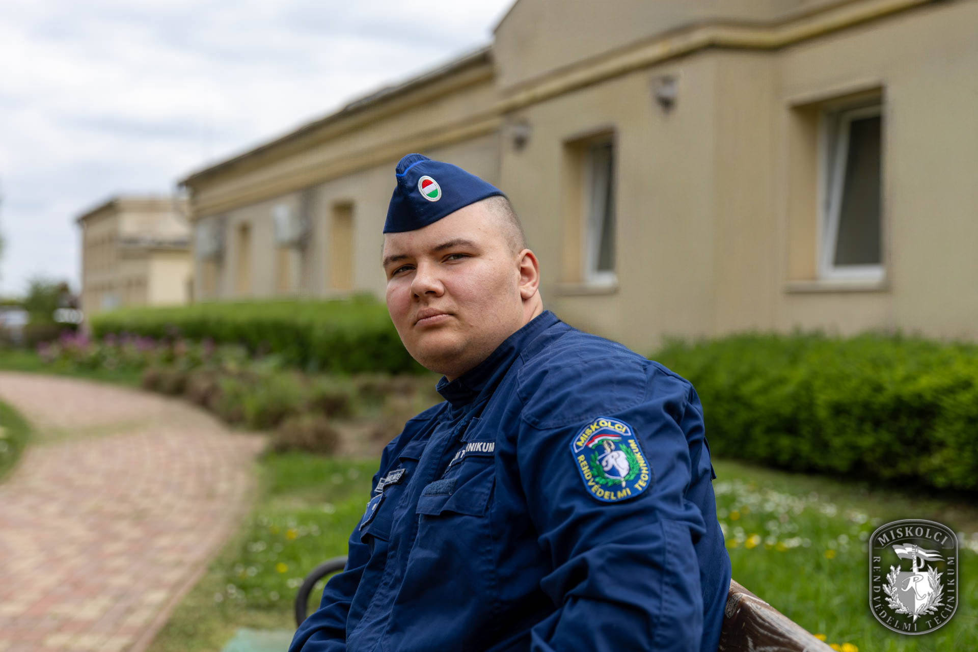 Dániel az iskola díszparkjában, egyenruhában ül egy padon.